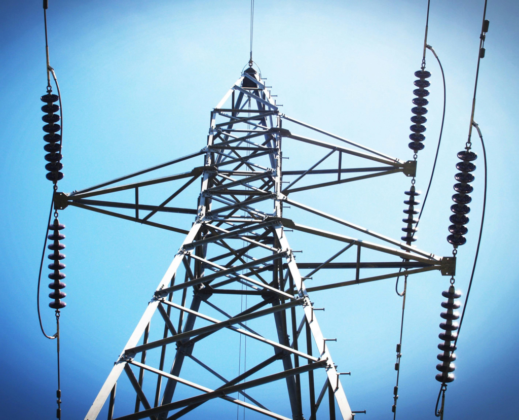 Low angle view of an industrial power transmission tower against a clear blue sky.